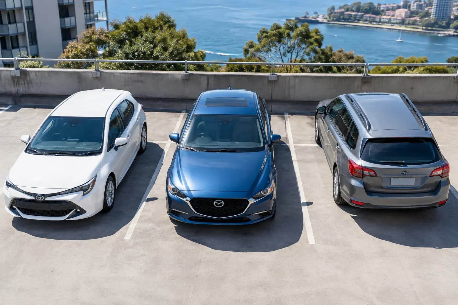 Three modest vehicles, sedan hatchback and wagon, parked in separate bays of a concrete car park