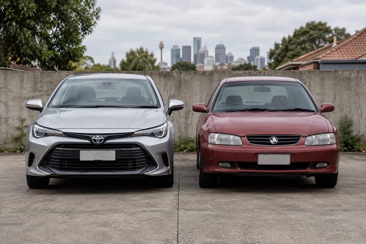 Two practical cars of clearly different ages parked side-by-side in a bare concrete courtyard