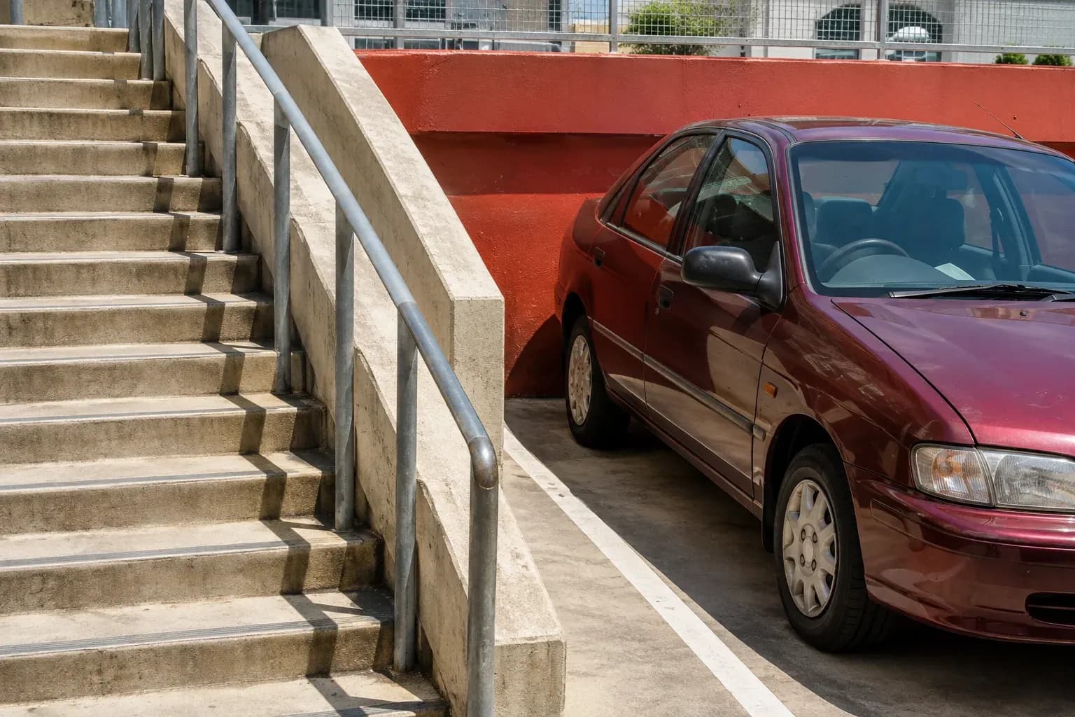 Steep concrete stairs beside a modest parked burgundy car in an urban car park