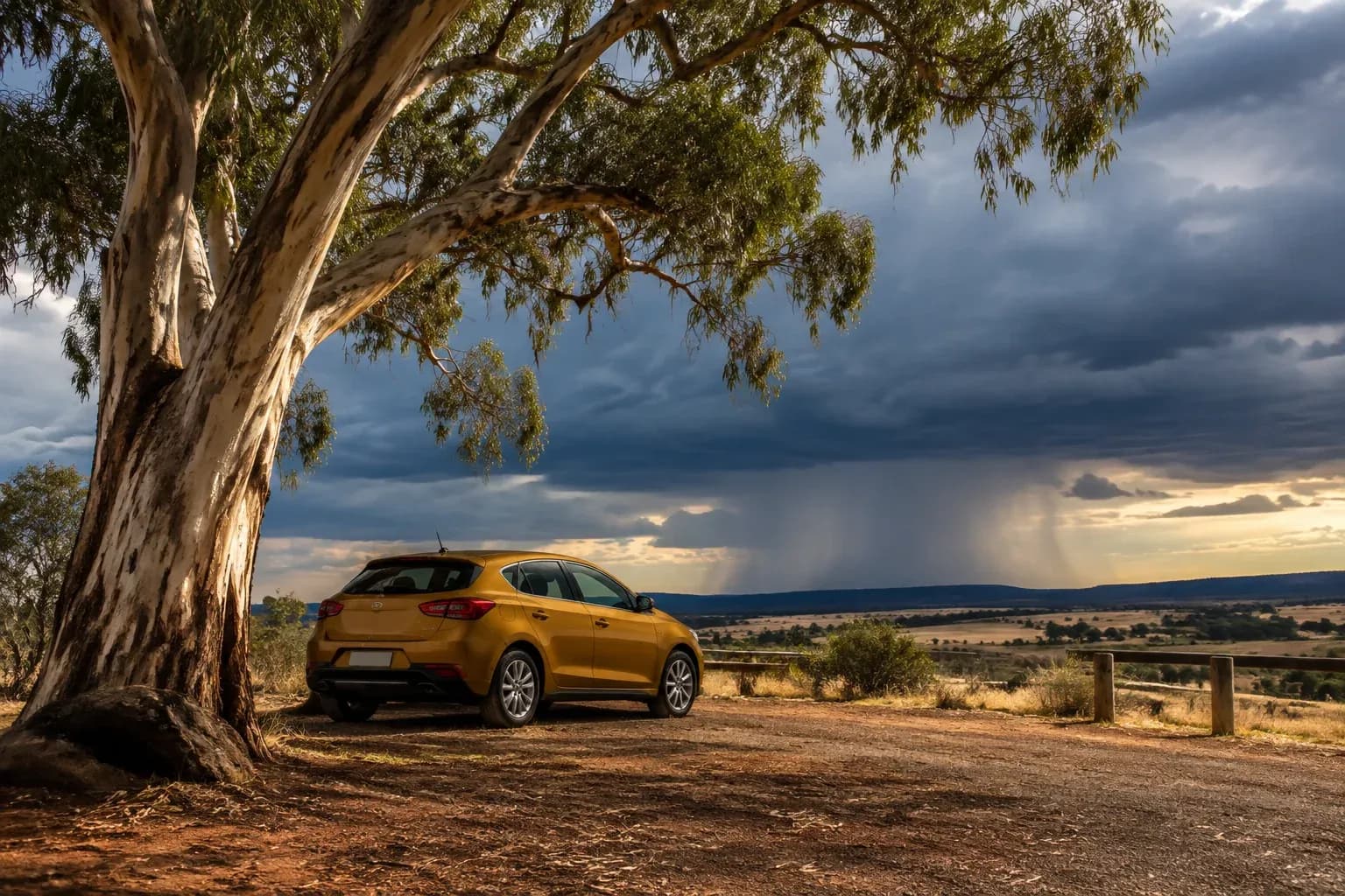 A lone ochre hatchback parked beneath a huge eucalyptus tree before a distant rainstorm, Australian country rest stop